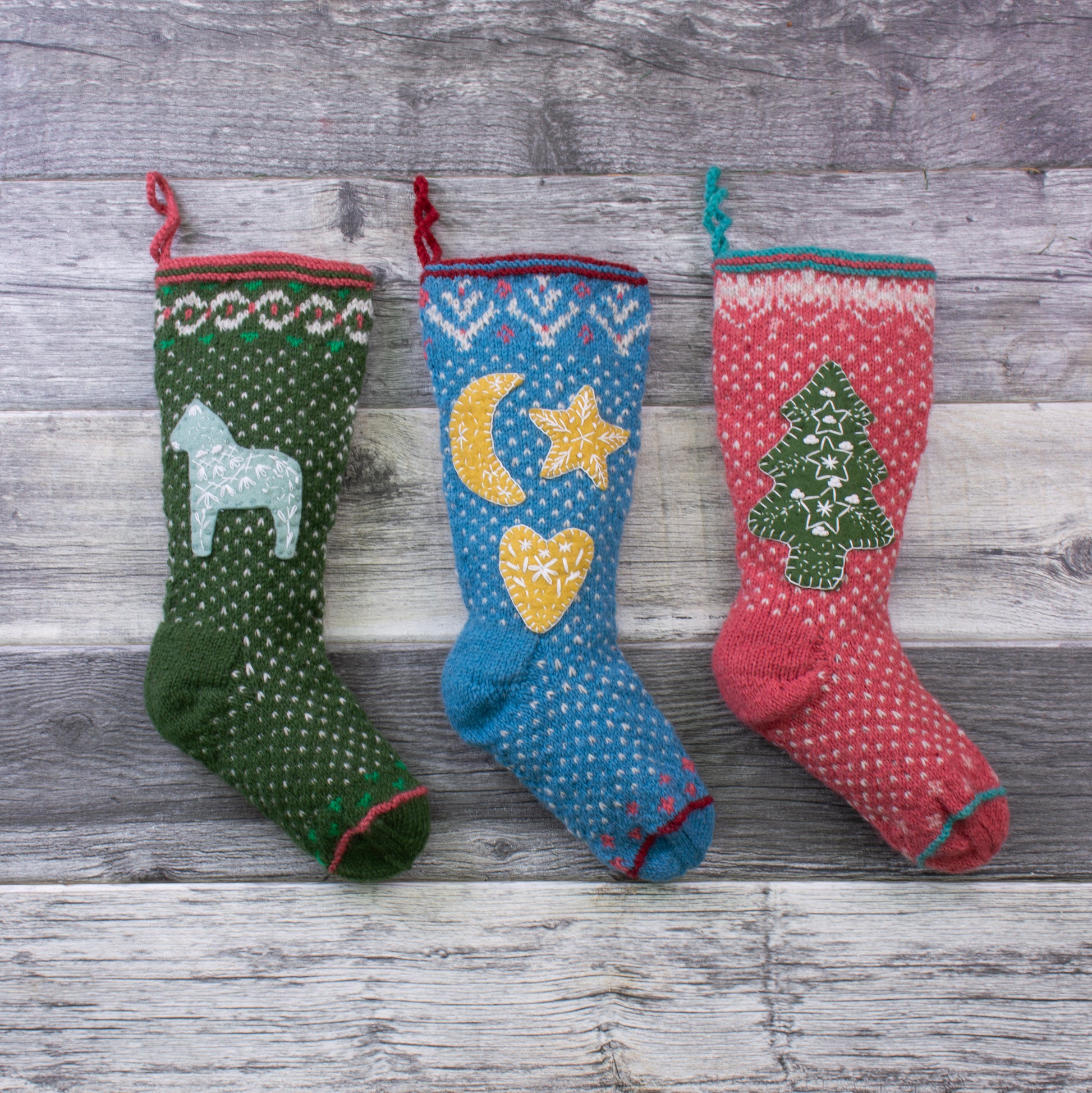 Hand-knit wool Christmas stockings with Dala horse, moon and star, and evergreen tree appliqués, Fair Trade and handmade in Nepal.